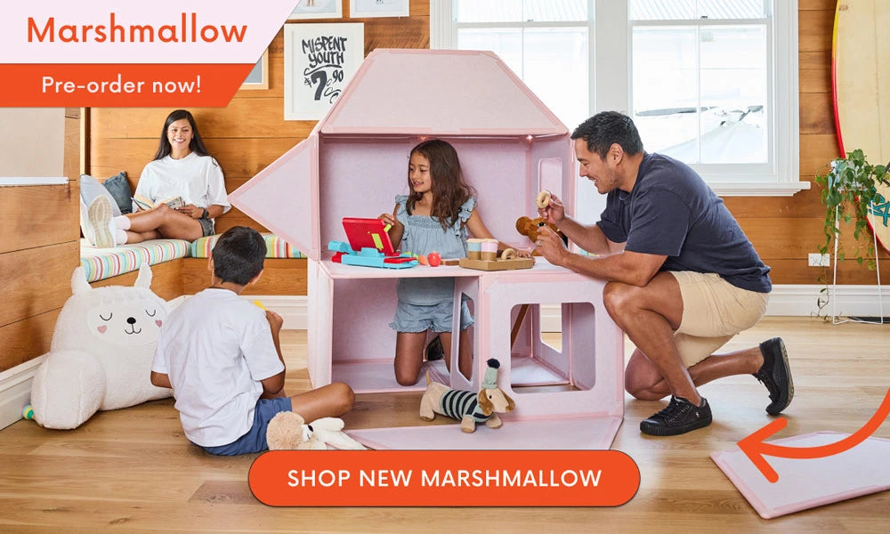 Family playing with a pink playhouse in a room with wooden flooring and large windows.